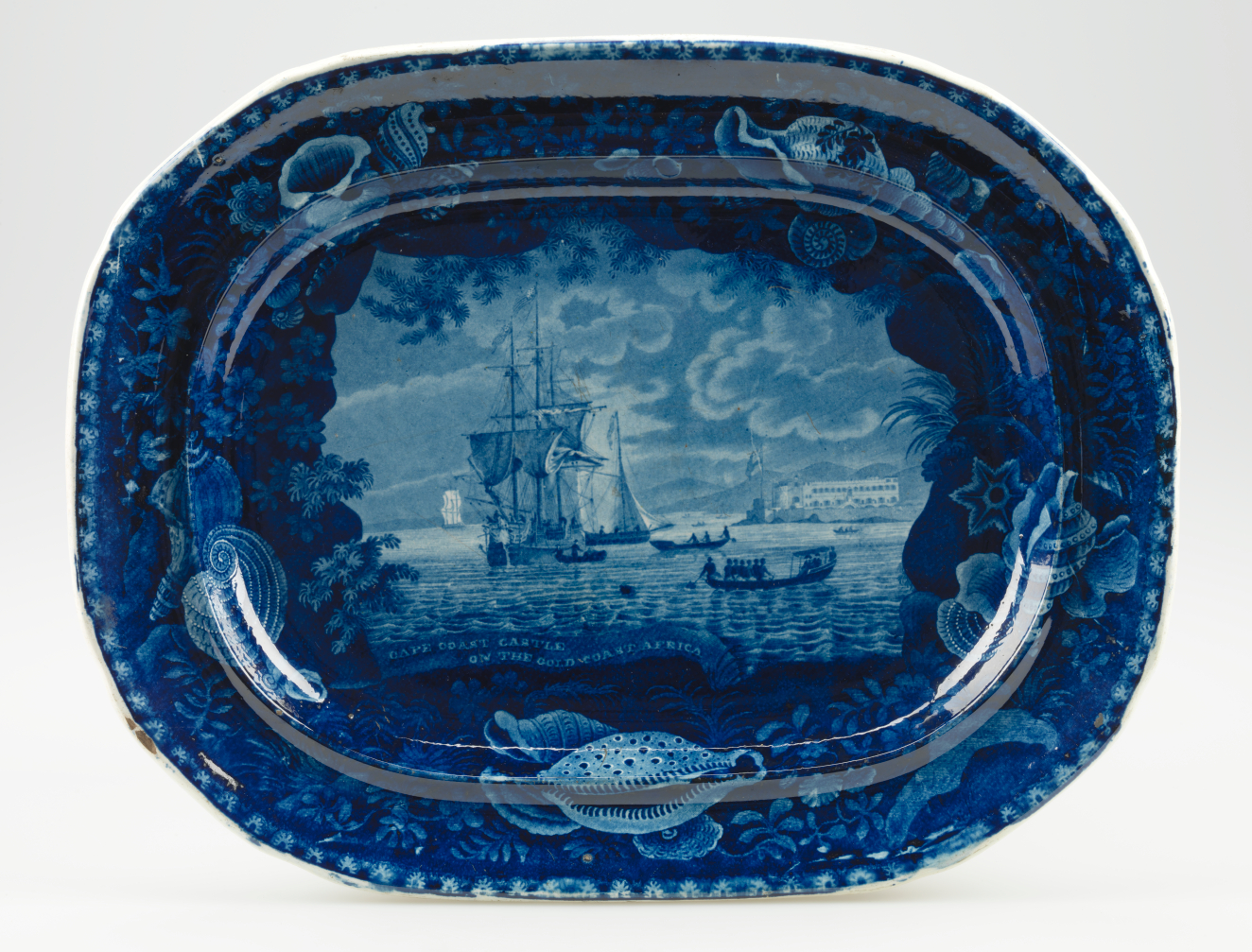A deep blue ceramic platter with a central illustration of a large ship, framed by a border of seashells, coral, and marine motifs.