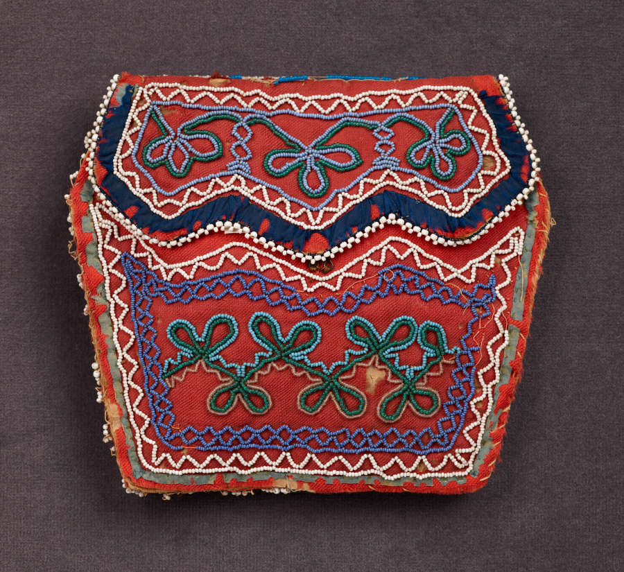 Red irregular hexagonal bag with a jagged flap. Wavy triangular patterning in whites and blues are beaded around the border with green knot-like motifs inside.