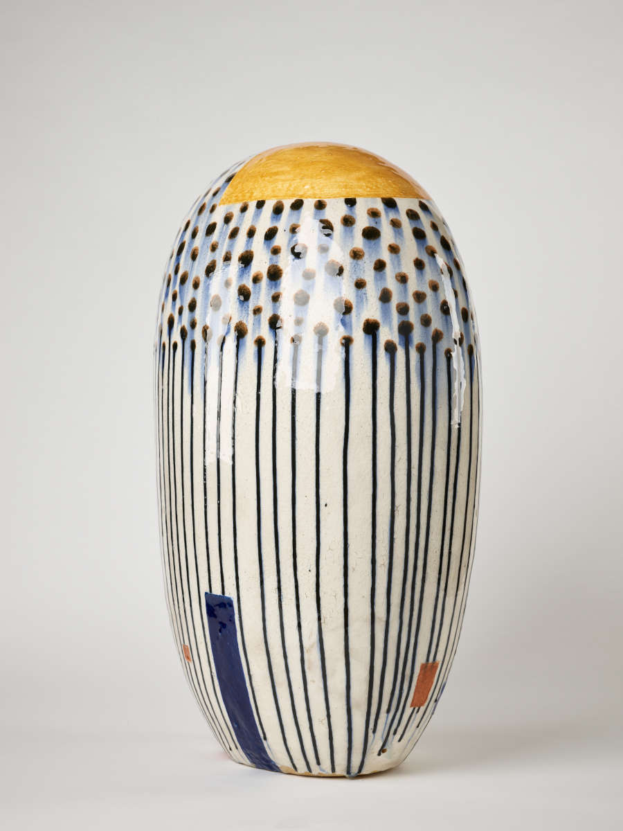 Tall, oval-shaped form glazed in white with smudged black dots that drip to form stripes. Sporadic yellow ochre squares and a blue rectangle decorate the bottom.