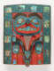 Wooden carving of a face with hands holding onto a deer’s antlers, painted in reds, blues, and ochres. It is framed by a turquoise border patterned with iridescent shell inlays.