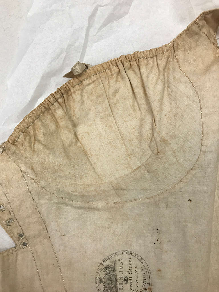 Close-up of slightly discolored cream fabric garment with gathered neckline and faded black ink maker’s stamp. 