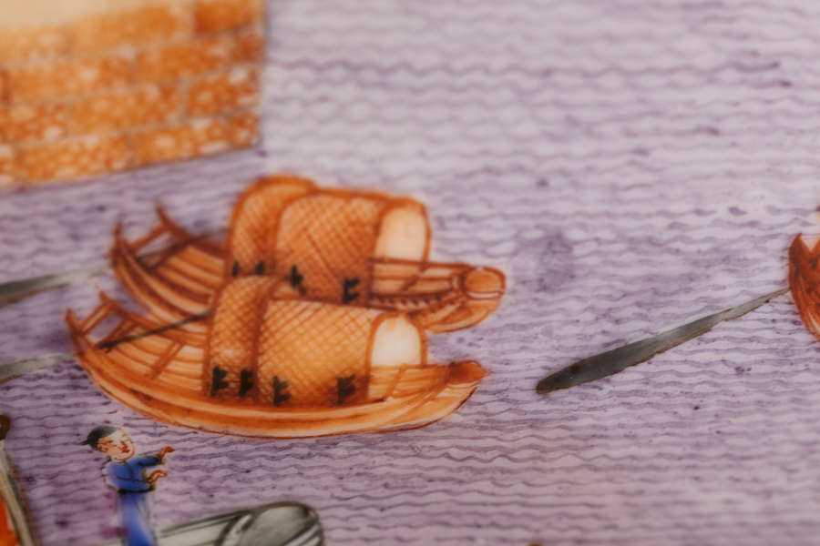 A close-up of a painted ceramic bowl depicting two wooden boats with woven coverings floating on purple water and a figure dressed in blue in the foreground.