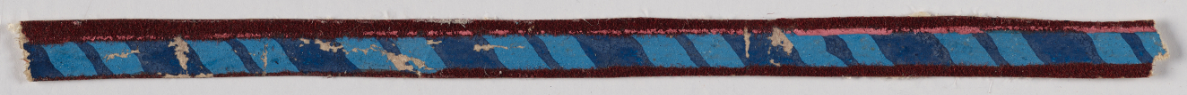 Thin horizontal strip on a light background in blue featuring light blue diagonal striping and dark red edges. The surface has small amounts of damage across the surface.