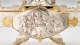 Close-up of a silver oval relief panel depicting a central flowing-robed man surrounded by cherubs, vines, and swirling drapery, enclosed in a gold-trimmed frame. 