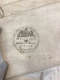 A close-up of an old textile with faded black ink stamp in a circular design and text reading “Inventor of the Patent Telima Corset. Mills Junr, Holywell Street, Strand, London.”