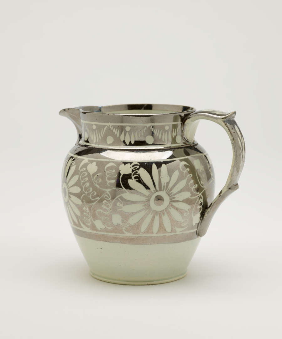 A silver-colored jug with floral motifs on the body of the vessel.