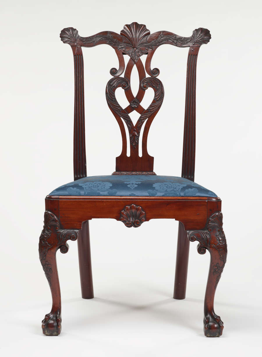 An intricately carved wooden chair with an open back and a blue upholstered seat supported by clawed feet.