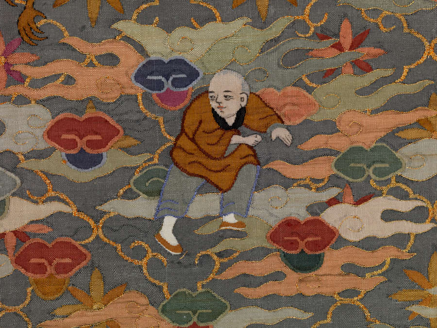 Section of illustrations on the blue robes back, featuring a latticed floral pattern overlaid with orange, green and blue wispy clouds. A monk in yellow and gray clothes sneaks around.
