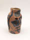 Asymmetrical clay vessel in warm pink tones with a small opening on its side, its uneven rim and subtly lopsided form painted with abstract blue and black geometric designs.