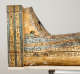 Side view of a coffin's foot, decorated with painted hieroglyphs and a painted depiction of a small reclining sphinx figure by the base.