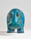 Front view of a bright turquoise hippopotamus decorated with black line work, the glossy surface showing patches of wear and evidence of age, revealing the clay underneath the turquoise glaze.