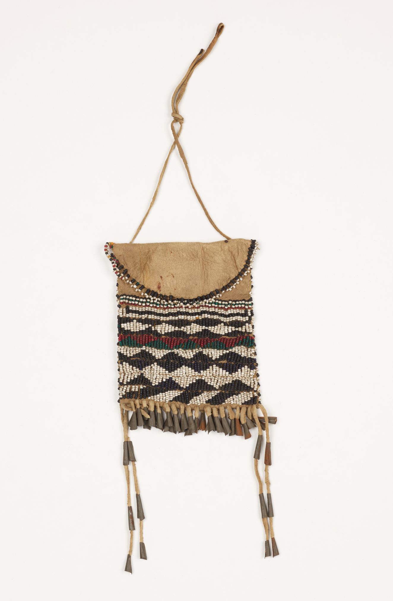 A leather beaded pouch with white, black, red, and green beaded designs. There is a handle as well as fringes with metal and leather decorations.
