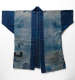 Faded indigo jacket with visible hand-stitched repairs and patchwork, with lighter center panels and darker blue sleeves.