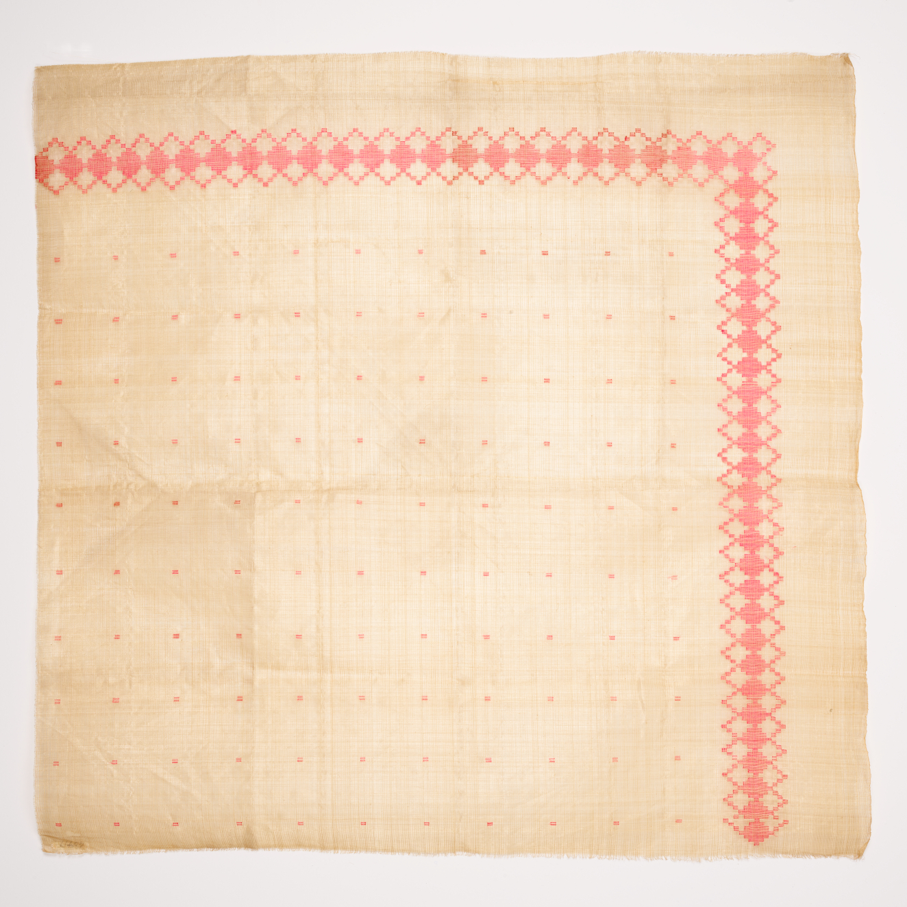 Beige square of woven fabric with various creases on a light background. Adorned with a pink diamond border along its top and right surrounding a subtle grid of pink dots.