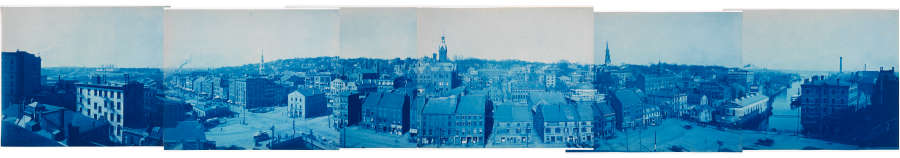 A blue-tinted panorama consisting of six different images overlaid on one another depicting a sprawling urban landscape with dense, old-world architecture, towering steeples, and streets from a bygone era.