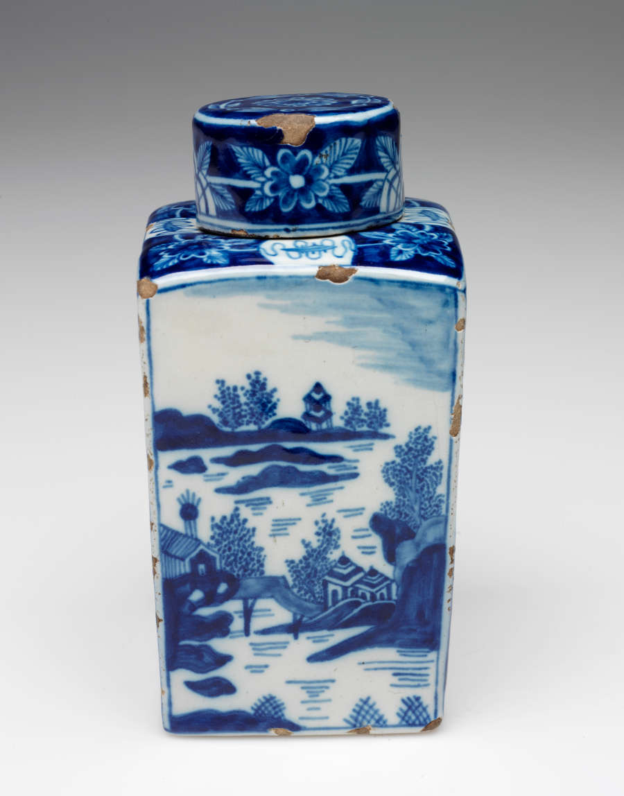 A rectangular vessel with blue and white architectural, landscape, and floral decorations. The lid is circular and with floral decorations.
