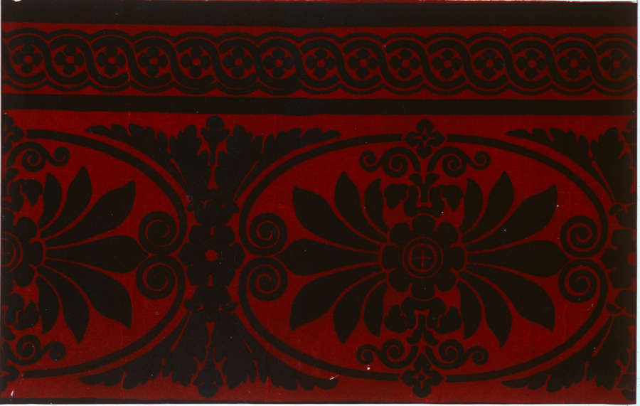 Black floral ornamentation in oval shapes with intricate scrolls on a deep red background. A thinner section of interwoven circles sits at the top.