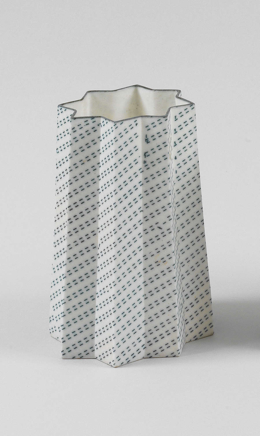 A tall, star-shaped vessel with eight points, its panels decorated with diagonal rows of dashes and black that wrap around the structure. 