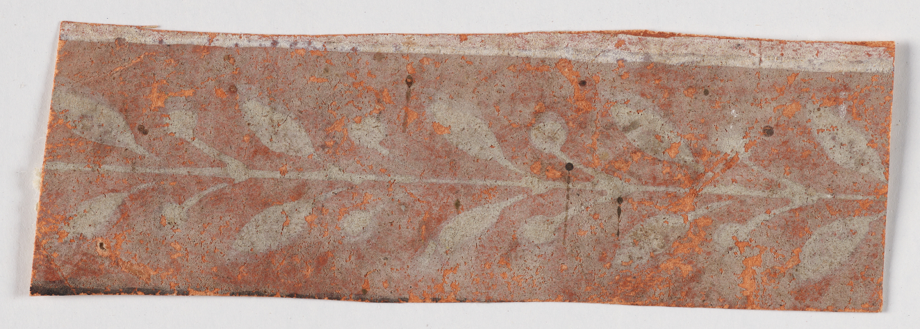 Horizontal decorative design on weathered, speckled orange surface featuring a faded white symmetrical leafy stem design below a light strip.