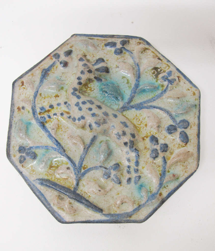 White octagonal tile with relief of intricate, flowing dark and light blue floral patterning overlaid with a stippled form of a gazelle at its center and bordered in blue.