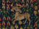Woven tapestry detail featuring a small golden deer-like creature leaping among vibrant floral patterns of red, green, blue, and yellow.