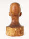 Back view of a glossy wooden bust depicting the head of a  male figure. The wood is cracked while retaining smooth contours, it also features carving marks and color variation.