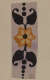 Vertical decorative strip featuring a yellow flower with a black center and lighter highlights, surrounded by  symmetrical black leaves and a vertical line of black dots on a neutral backdrop.