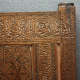 A close up view of a carved wooden panel with intricate calligraphic designs surrounded by decorative floral carvings and interwoven geometric star designs.