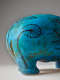 Close view of a turquoise hippopotamus figurine showing black floral linework across the back leg, the glossy blue surface marked by thin cracks showing the clay underneath the glaze.