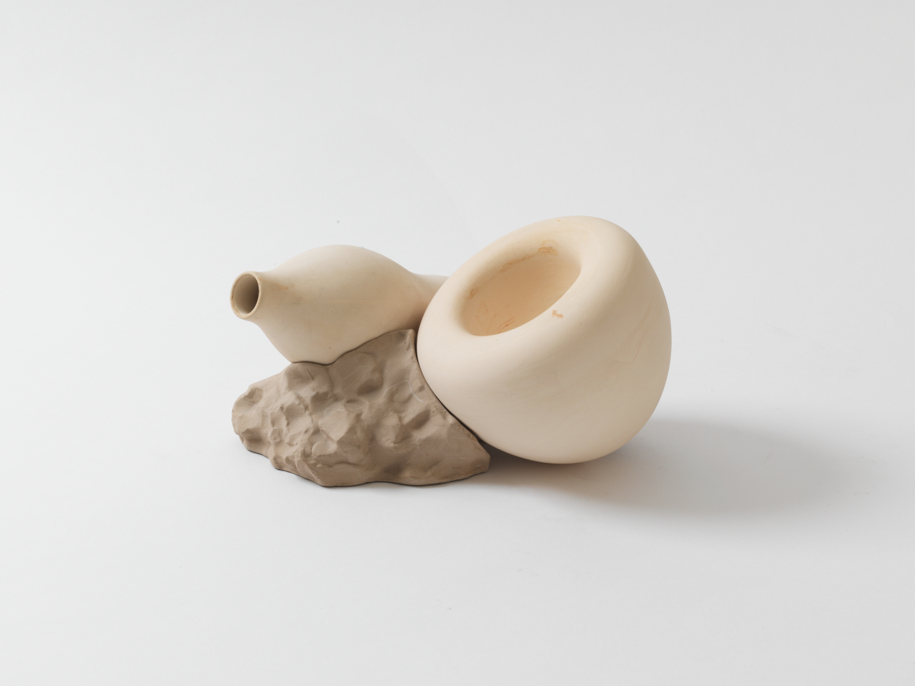 A sculptural piece with two cream-colored bulbous forms resting on a stone-like base.