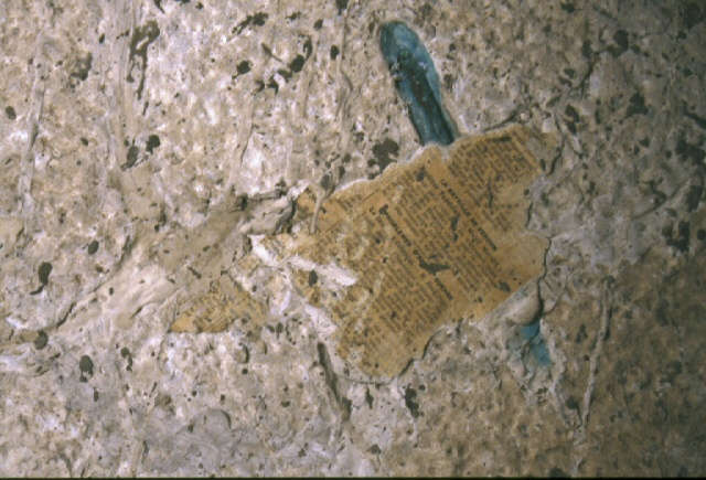 A fragment of aged printed text embedded into a rough, cracked surface with streaks of blue pigment. 