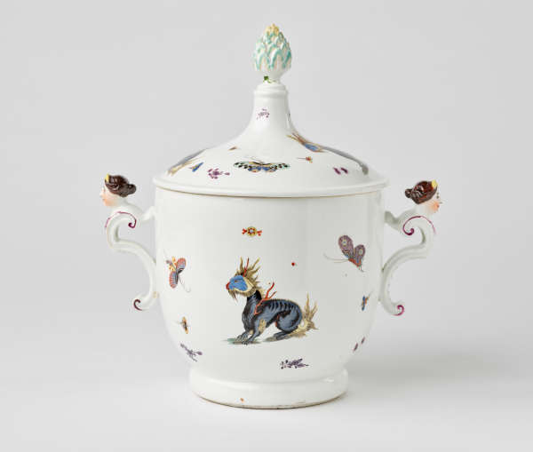 A white lidded vessel with dragons and bugs decorations. There are two sculptural handles with figure’s heads at the top. Finial has light green, leaf-like decorations.