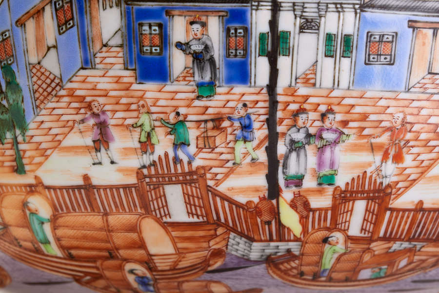 A close up depicting a bustling harbor scene with boats in the foreground, people walking near a wooden fence, and vibrant blue buildings with decorative windows.