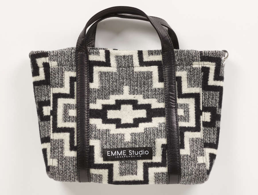 Gray tweed purse with black and white geometric patterning and one black leather handle on the front and back. A black brand label with white text in the center reads, “EMME Studio. Lenapehoking.”