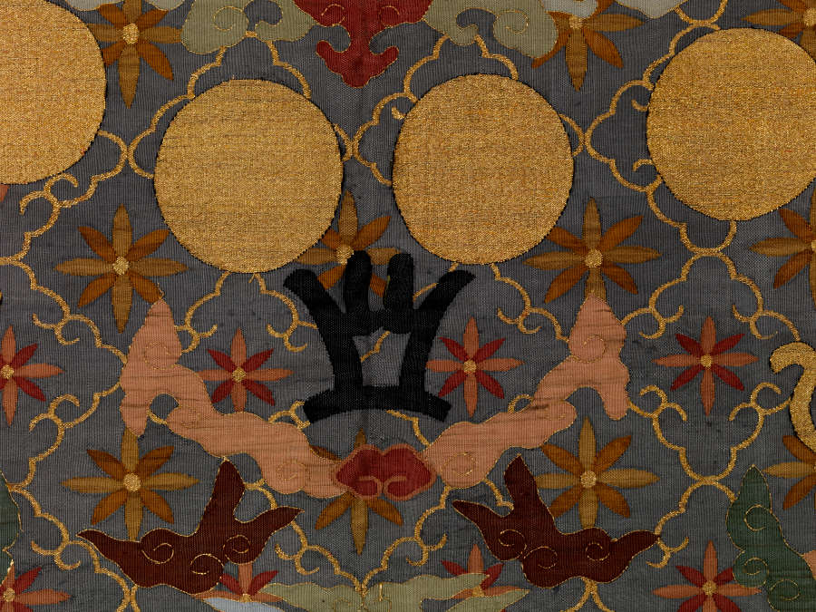 Detail of the robe, showing four golden circles and symmetrical black and pink forms against a dark background with a golden diagonal grid pattern, within each square is a flower.