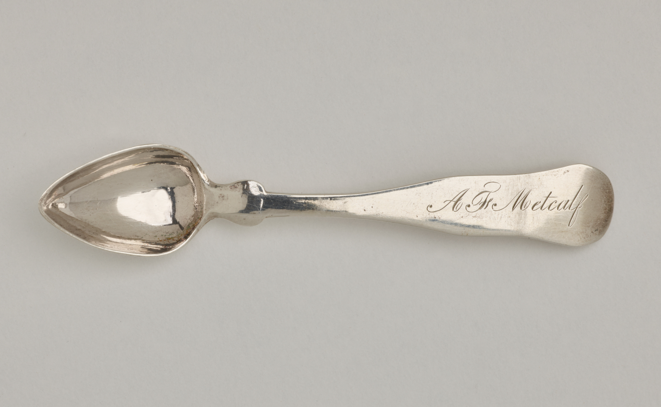 A silver salt spoon the bowl comes to a pointed tip, the neck is thin, and the handle is thicker and rounded at the end.
