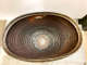 Top view of an oblong bowl in storage. It has a thick bronze rim and circular ridges. Its interior is dark orange blending into greens and whites near the center. 
