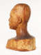 Three quarter back view of a glossy wooden bust depicting the back of the head of a  male figure. The wood features long vertical cracks, carving marks and color variation.