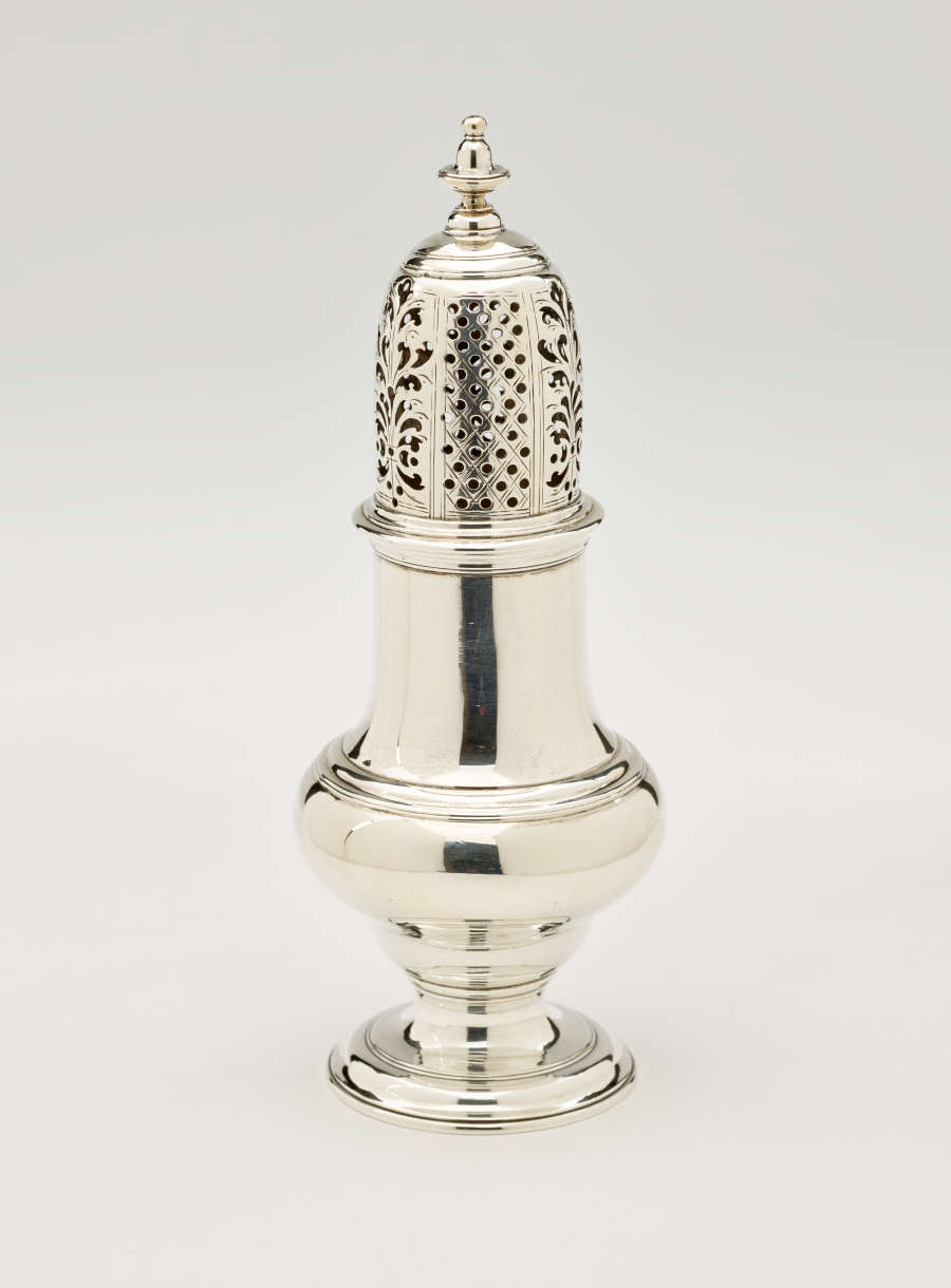 A silver vessel with a foot, rounded body that goes to a cylindrical top half, and the lid is perforated with small holes and floral cutouts.