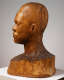 Back view of a carved wooden bust depicting the head of a male figure. The wood is cracked while retaining shine, the sculpture also features carving marks throughout.