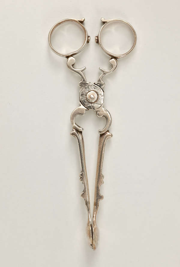 Silver sugar tongs that are delicate and swirled.