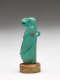 Side-view of the aquamarine sculpture of a nude anthropomorphic hippo-headed woman with bare breasts, long hair and arms, and sculpted loop on its back. It’s mounted on a stone disk.