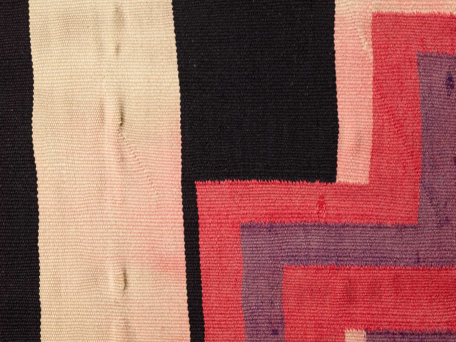 Rotated closeup view of a black and cream blanket with purple and pink cross designs throughout. Pinkish stains from the cross design seep into the adjacent cream stripes.