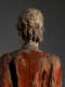 Close up of the back of a wooden statue's head, showing carved wavy blonde hair, red robes and visible signs of age.