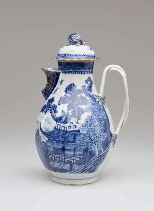 A white and blue chocolate pot with a spout, handle, and lid, the edges of the lid and spout are gilded. The decorations mainly depict floral, architectural, and landscape elements.