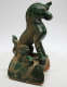 Side-view of a green and brown sculpture of a sitting horse with a fish-like tail. The horse is seated on a thick green platform with brown signs of wear. 