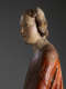 A profile view of a weathered wooden statue of a figure with a solemn expression, with red and green drapery.