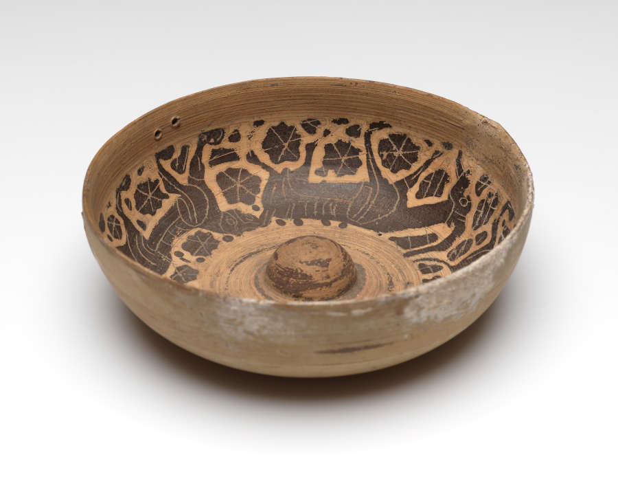 Angled side-view of a ceramic bowl with its internal walls decorated with black illustrations of animals and floral motifs. A small dome rises from the wide bottom of the bowl.