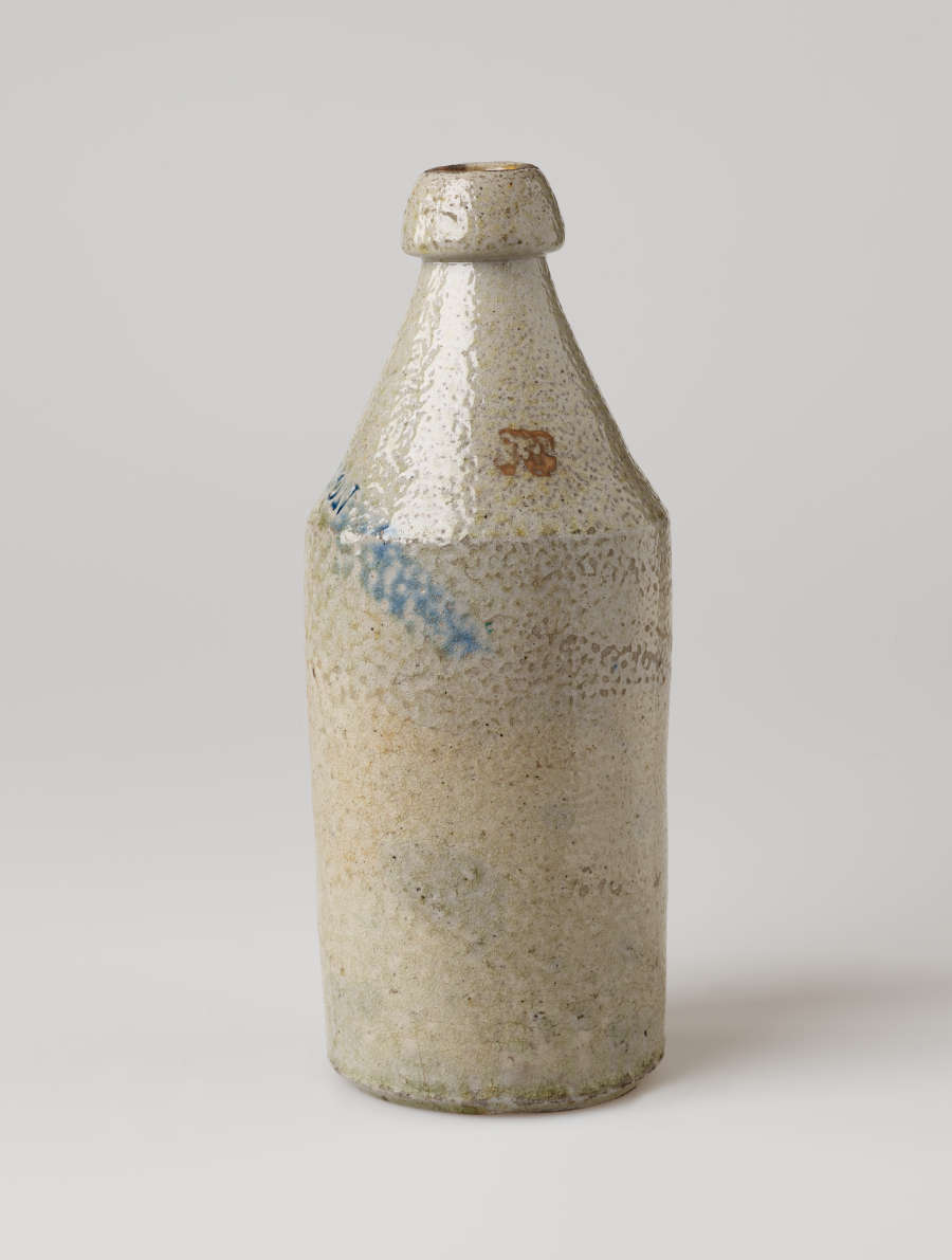 A cream ceramic bottle with a thick rounded lip tapering out to a cylindrical body. There is a dark rust colored spot and a blue line.
