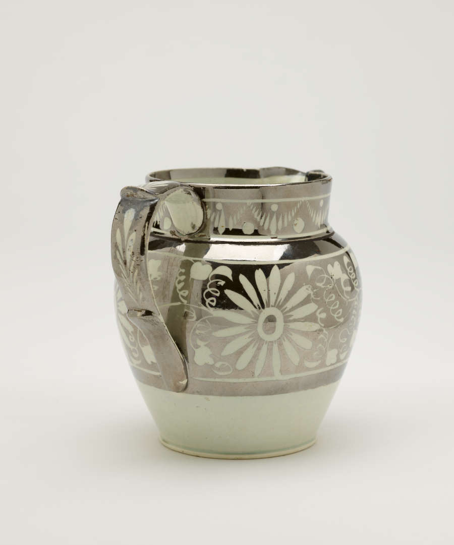 A silver-colored jug with floral motifs on the body of the vessel.